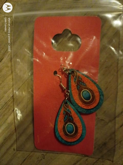 Pair of teardrop-shaped wooden earrings with a teal, orange, and black peacock feather eye pattern on a red background.